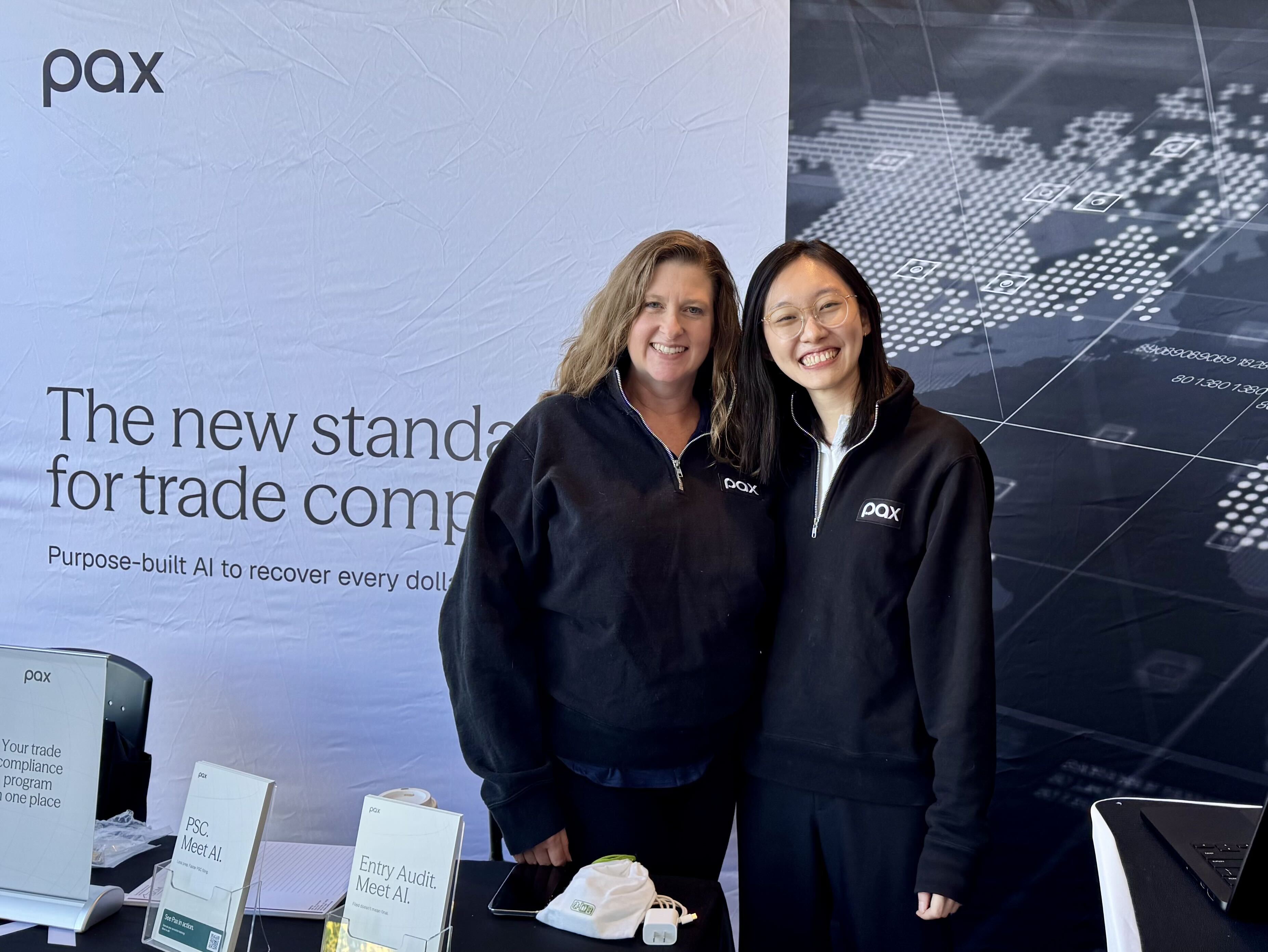 Two people wearing Pax jackets at a Pax event booth